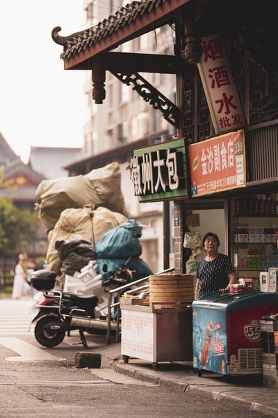 白天，一名身穿黑色夹克的男子站在食品摊旁